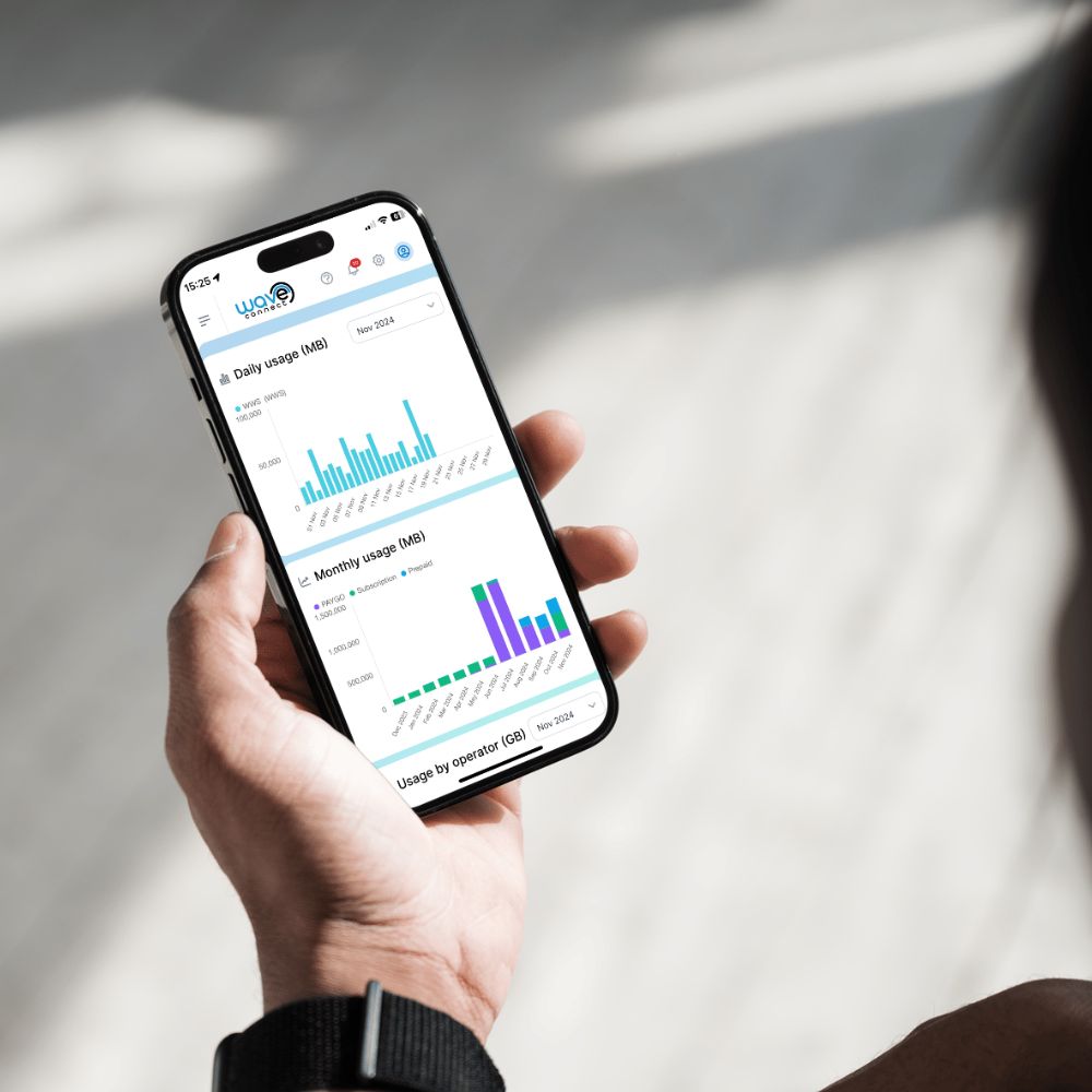 A person holds a smartphone showing a usage analytics dashboard with charts and graphs. The background is a softly blurred light gray surface with natural shadows.